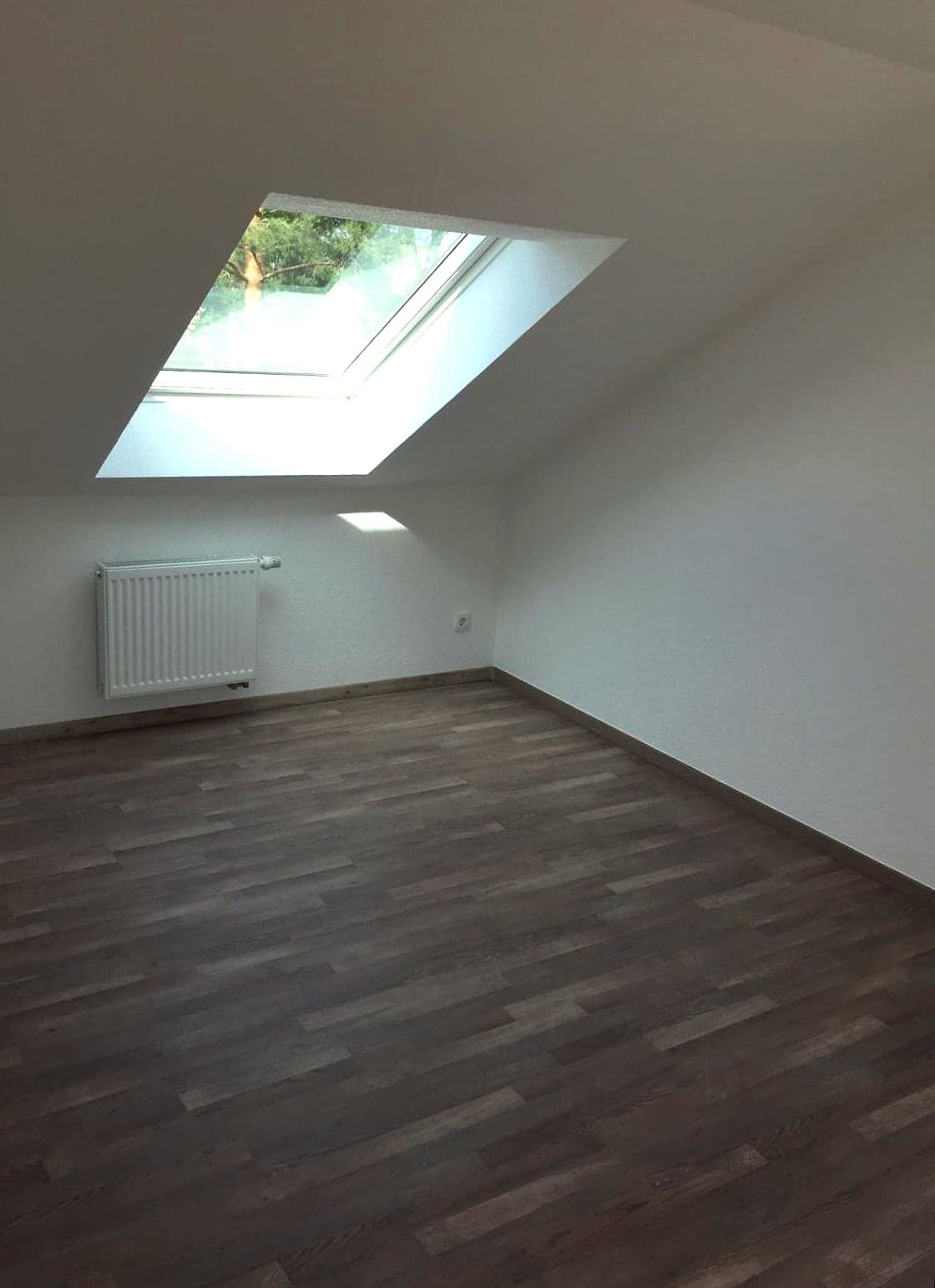 Renoviertes Dachzimmer mit Dachfenster, hellen Wänden und dunklem Holzboden
